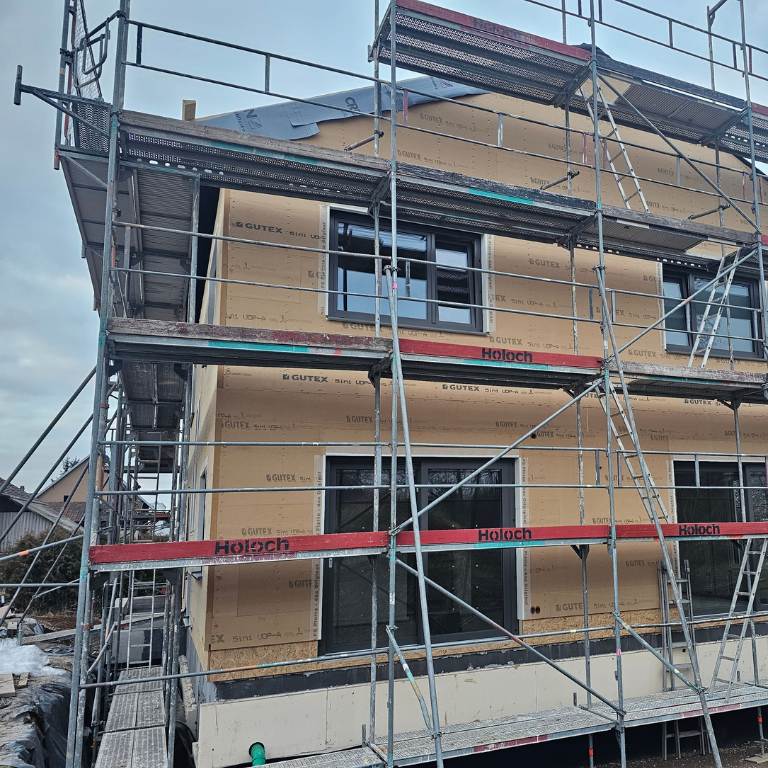 Holzfaser WDVS Fassade im Neubau, Frontansicht mit Gerüst und montierten GUTEX Dämmplatten